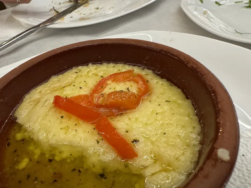 A clay dish of baked cheese topped with red pepper