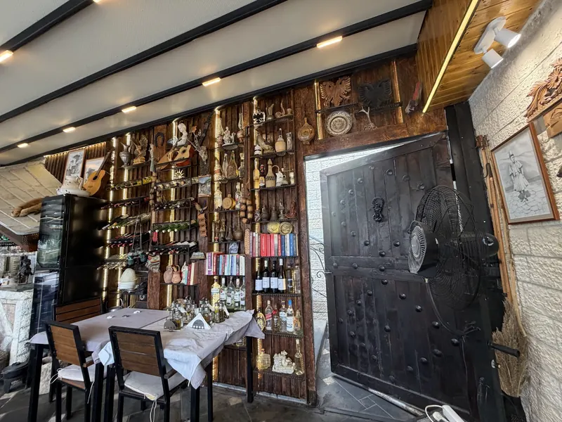 Dining room wall lined with old bottles, copper pots and folk objects next to a heavy wooden door